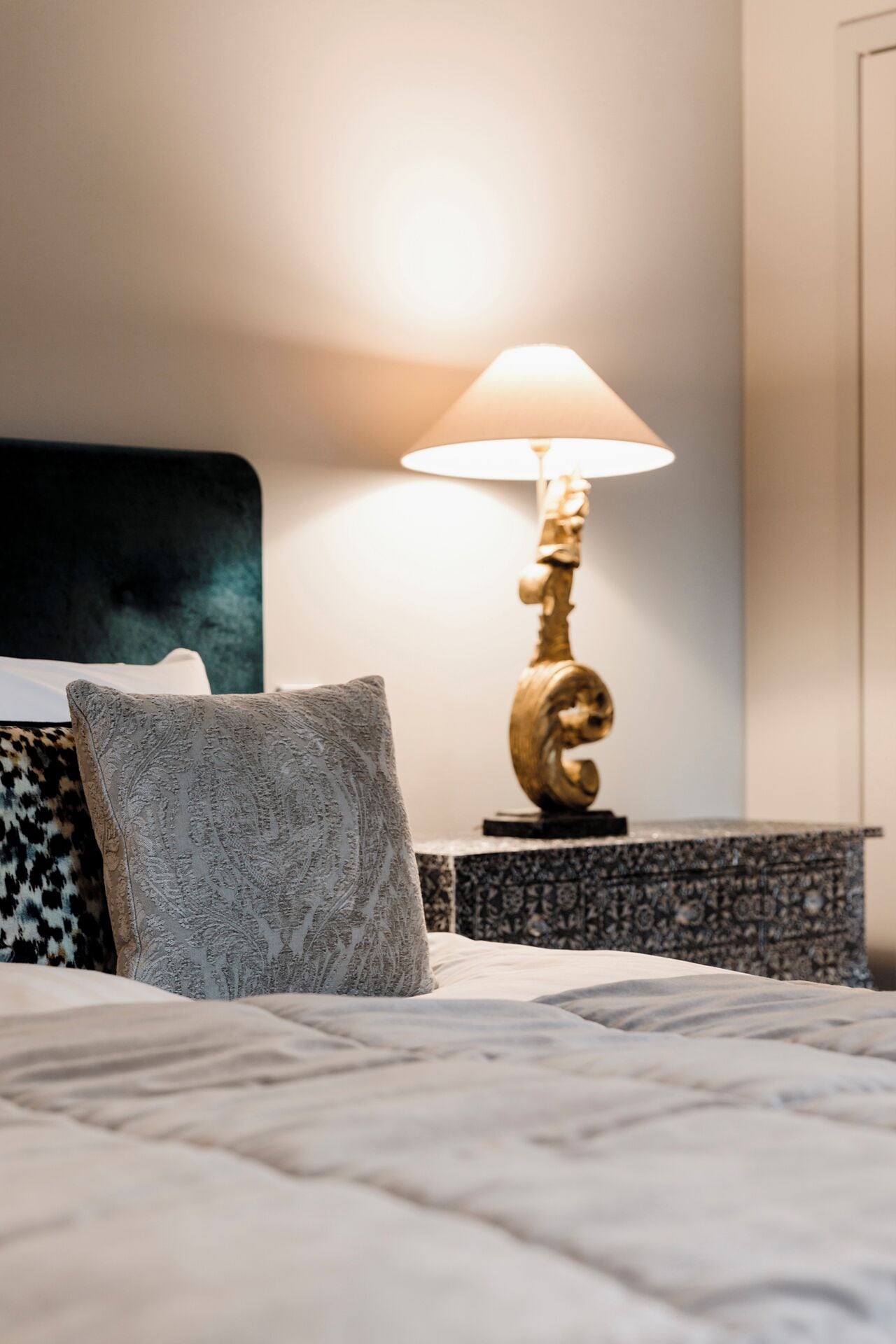 A neatly made bed with a patterned pillow, a decorative lamp, and a headboard.