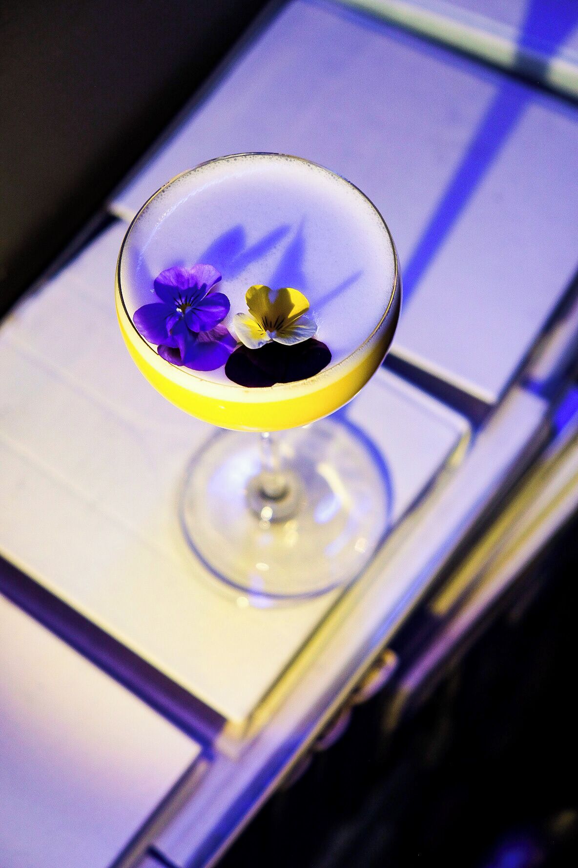 Una copa de martini con un borde amarillo y una guarnición floral sobre una mesa.