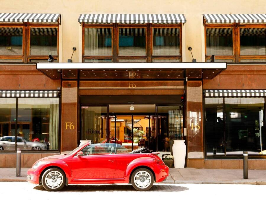 Entrada de hotel com um conversível vermelho clássico estacionado na frente.