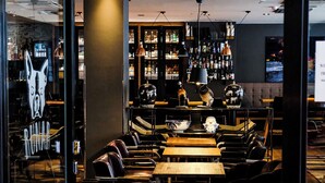 A bar area with leather chairs, tables, and a variety of bottles on shelves.