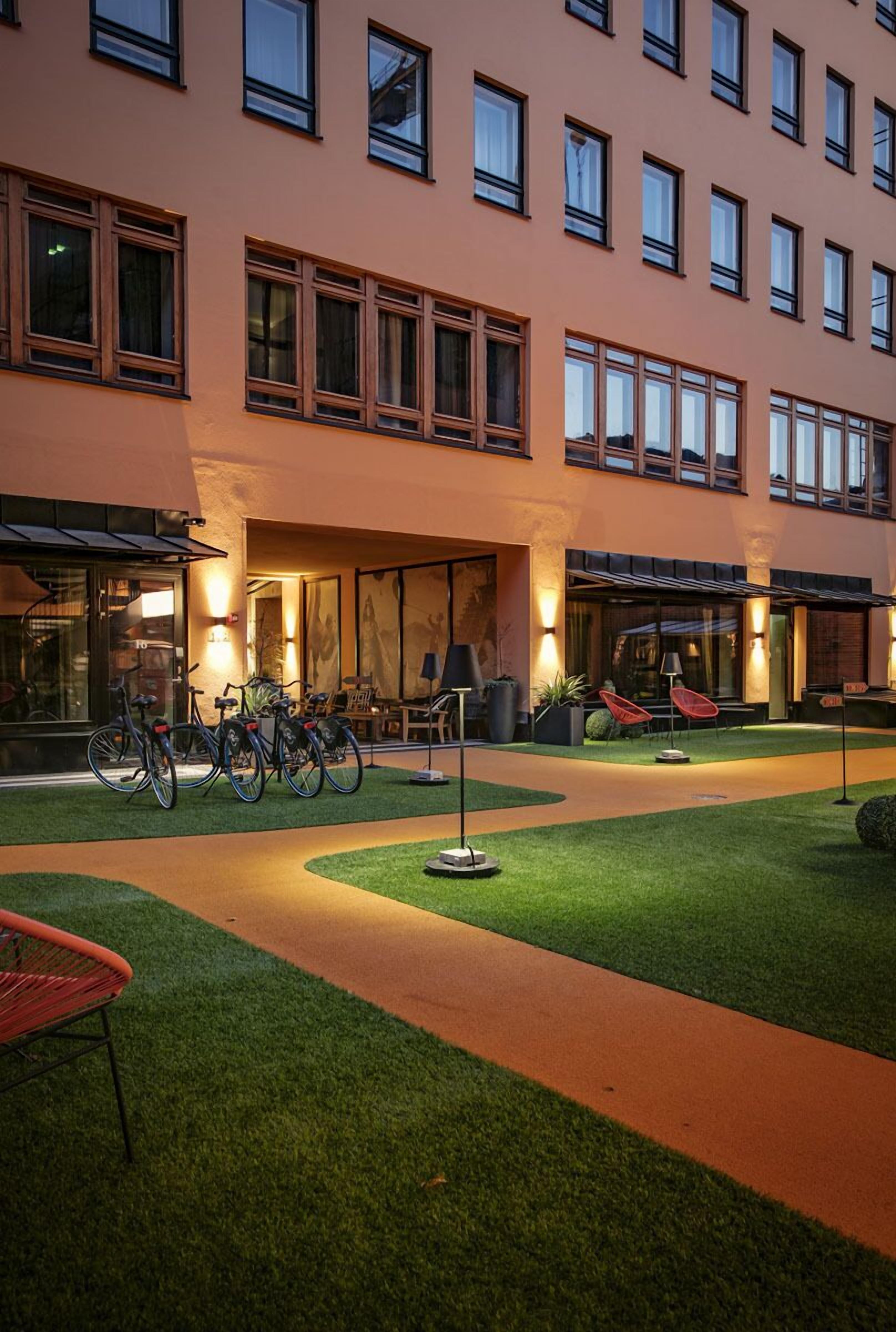 A hotel with a courtyard featuring bicycles, outdoor seating, and a well-lit entrance.