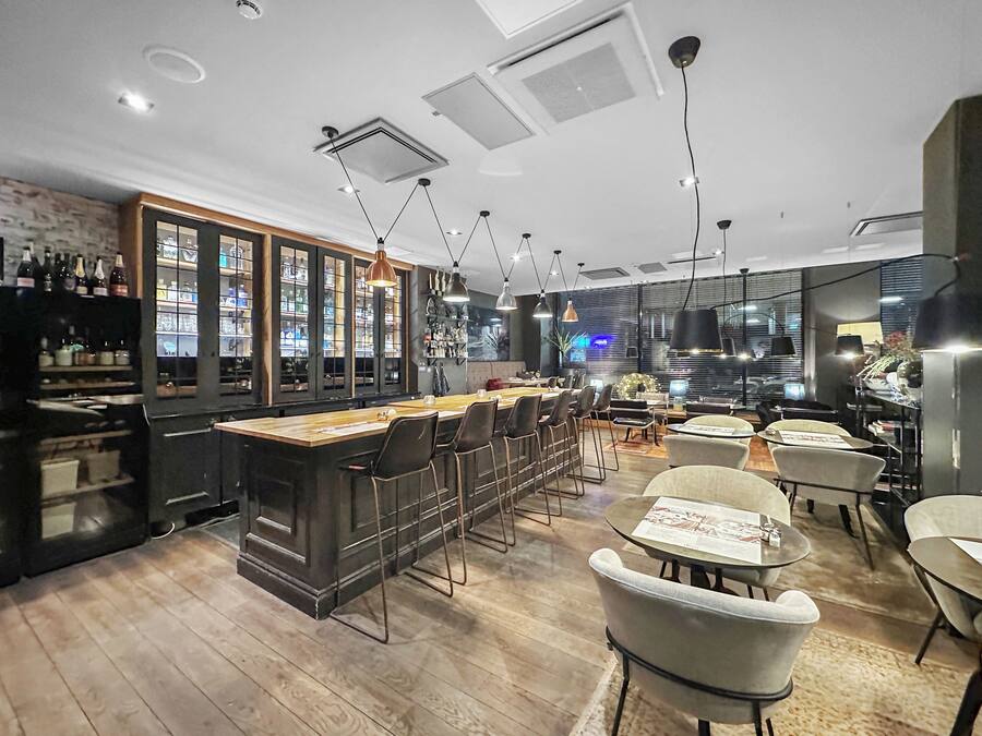 A modern bar area with a wooden bar counter, multiple bar stools, and pendant lighting.