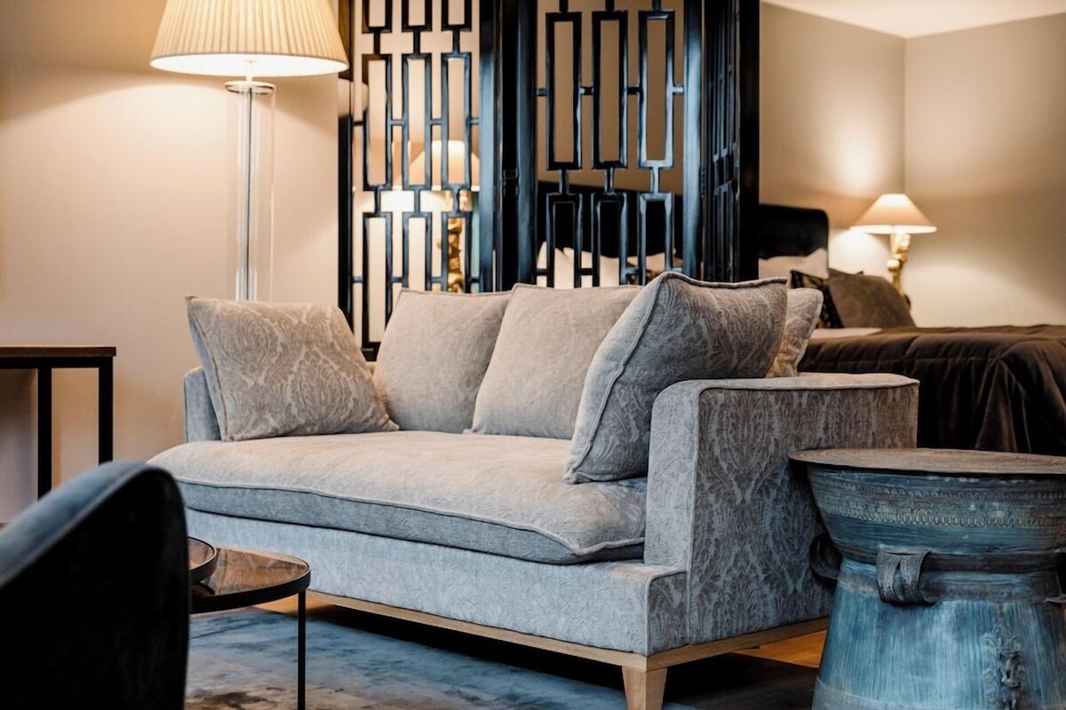 Un salón moderno con un sofá gris, una mesa de centro redonda y un panel decorativo en la pared.