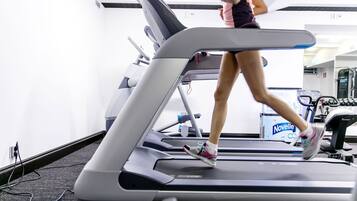 Una persona corriendo en una cinta de correr en un gimnasio, con una botella de agua Novelle visible al fondo.