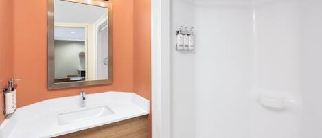 A bathroom with a white sink, a mirror with lights, and a shower area.