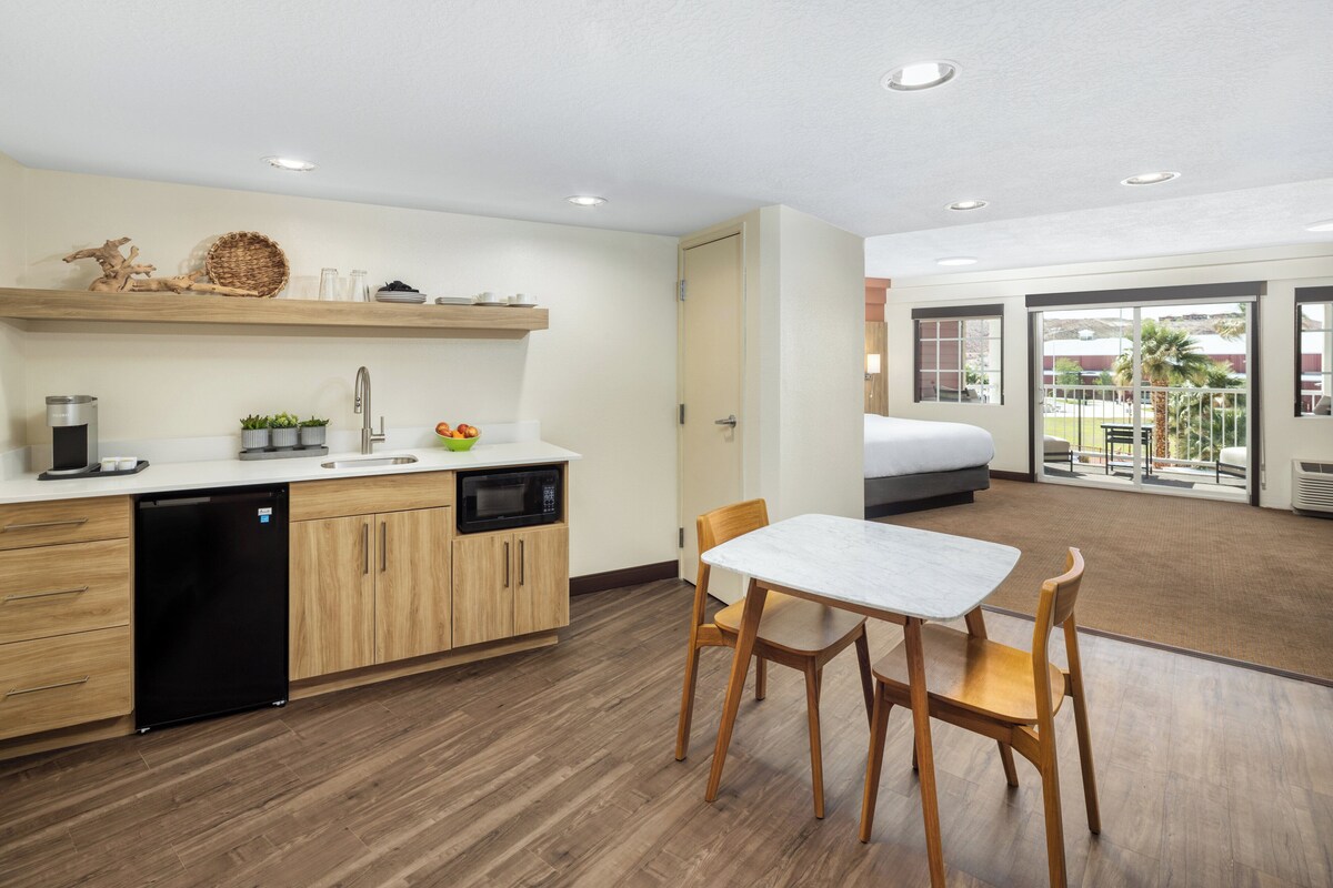 A modern kitchen with wooden cabinets, a dishwasher, and a microwave. There is a dining area with a table and chairs.