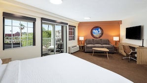 A hotel room with a large bed, a sofa, a desk, a TV, and a balcony with a view of the city.