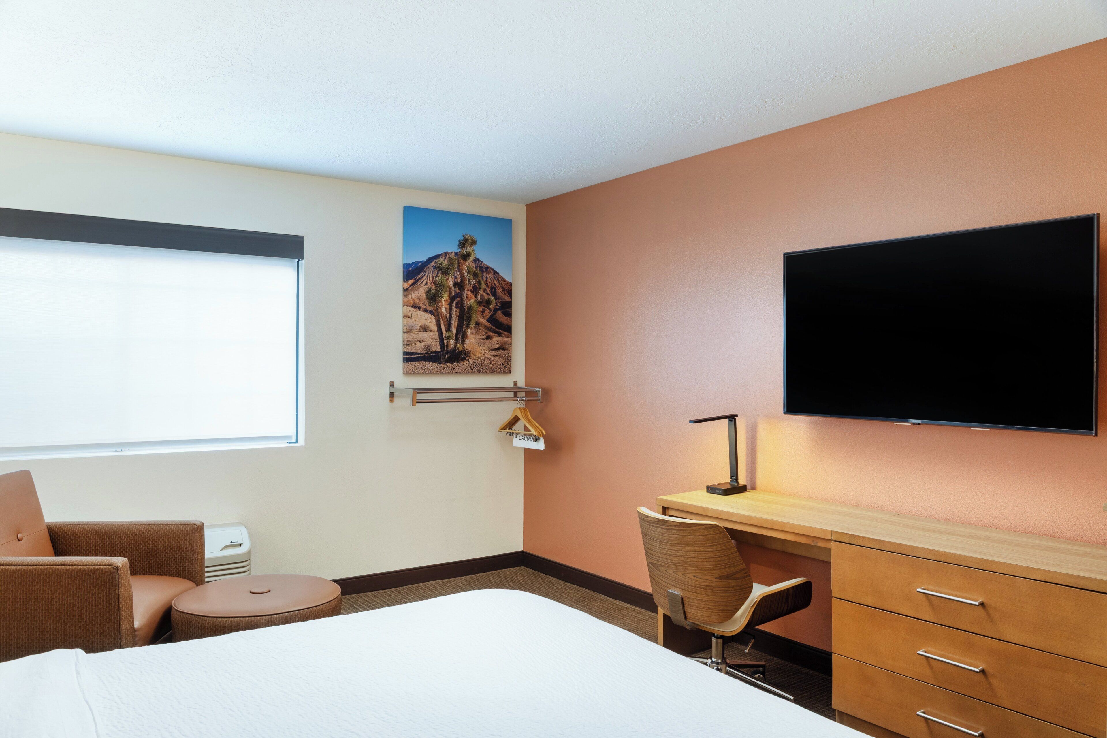 Una habitación de hotel con cama, escritorio, silla, televisor y ventana.