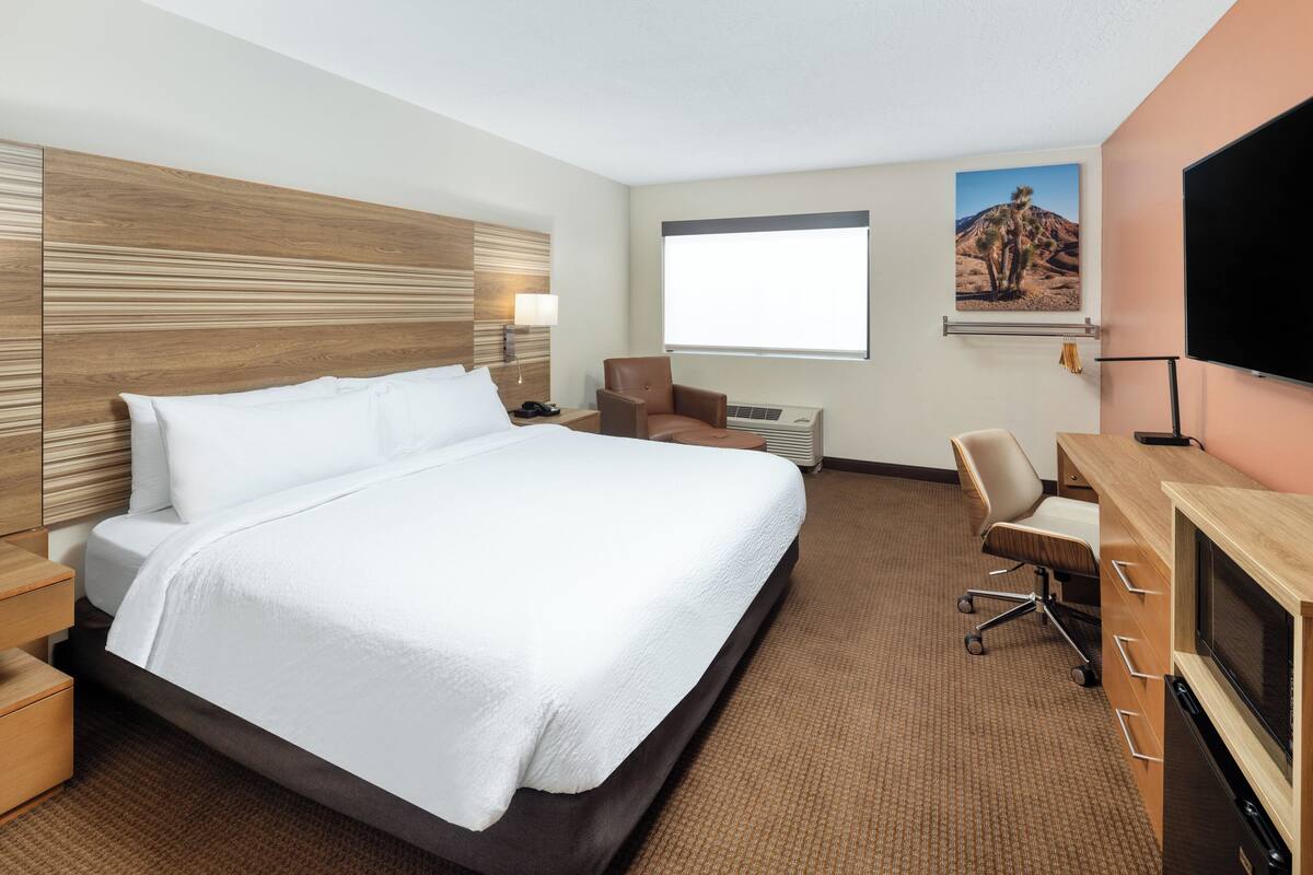 A hotel room with a large bed, a desk with a computer, a chair, a TV, and a window with a desert view.
