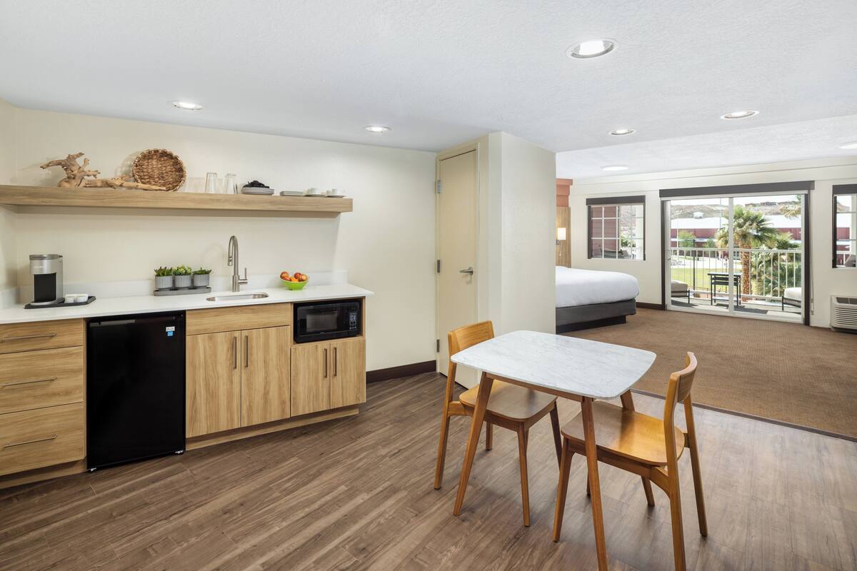 A modern kitchen with wooden cabinets, a dishwasher, and a microwave. There is a dining area with a table and chairs.