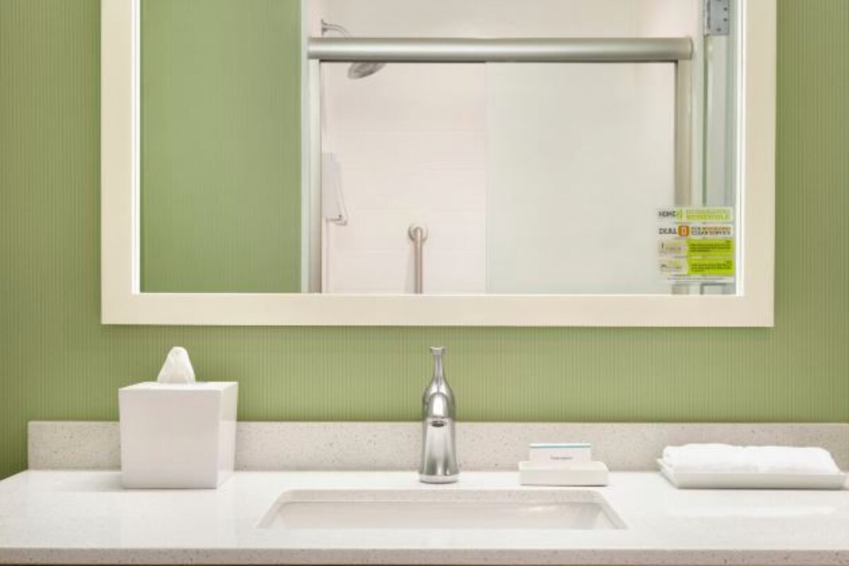 Un bagno con un lavandino bianco, uno specchio e un portascopevoli.