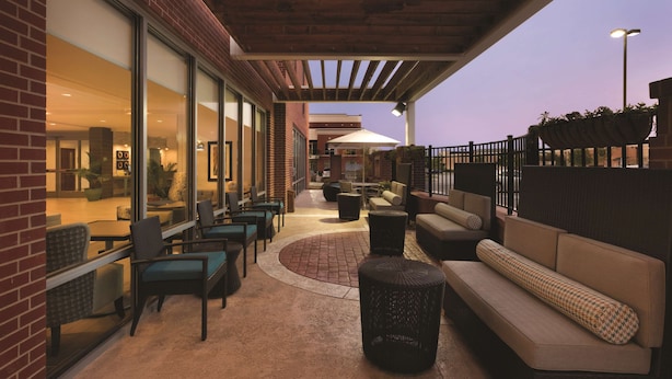 Un patio al aire libre con arreglos de asientos, un muro de ladrillo y una sección cubierta con una pérgola.