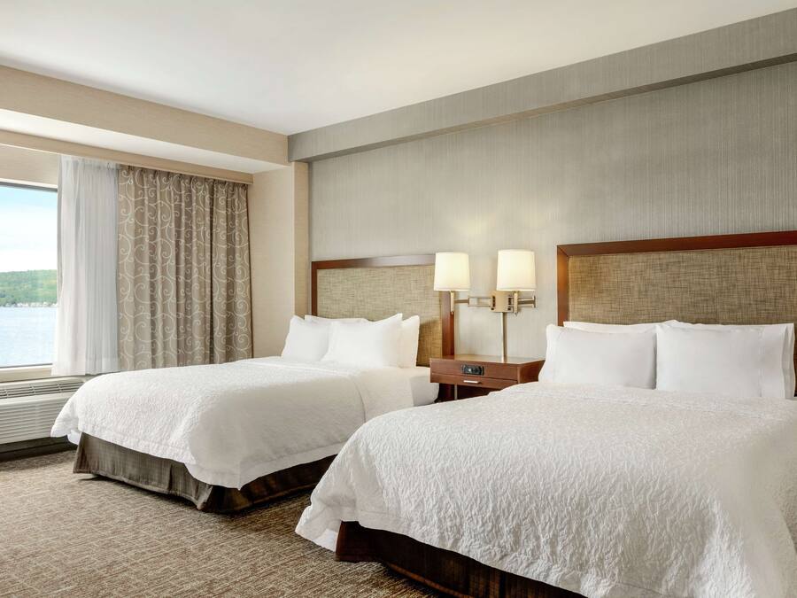 Habitación de hotel con dos camas, un ventanal con cortinas, vista al exterior y una lámpara fijada a la pared.