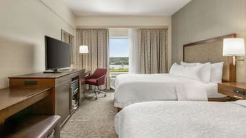 A hotel room with two beds, a desk with a TV, a chair, and a view of the outdoors.
