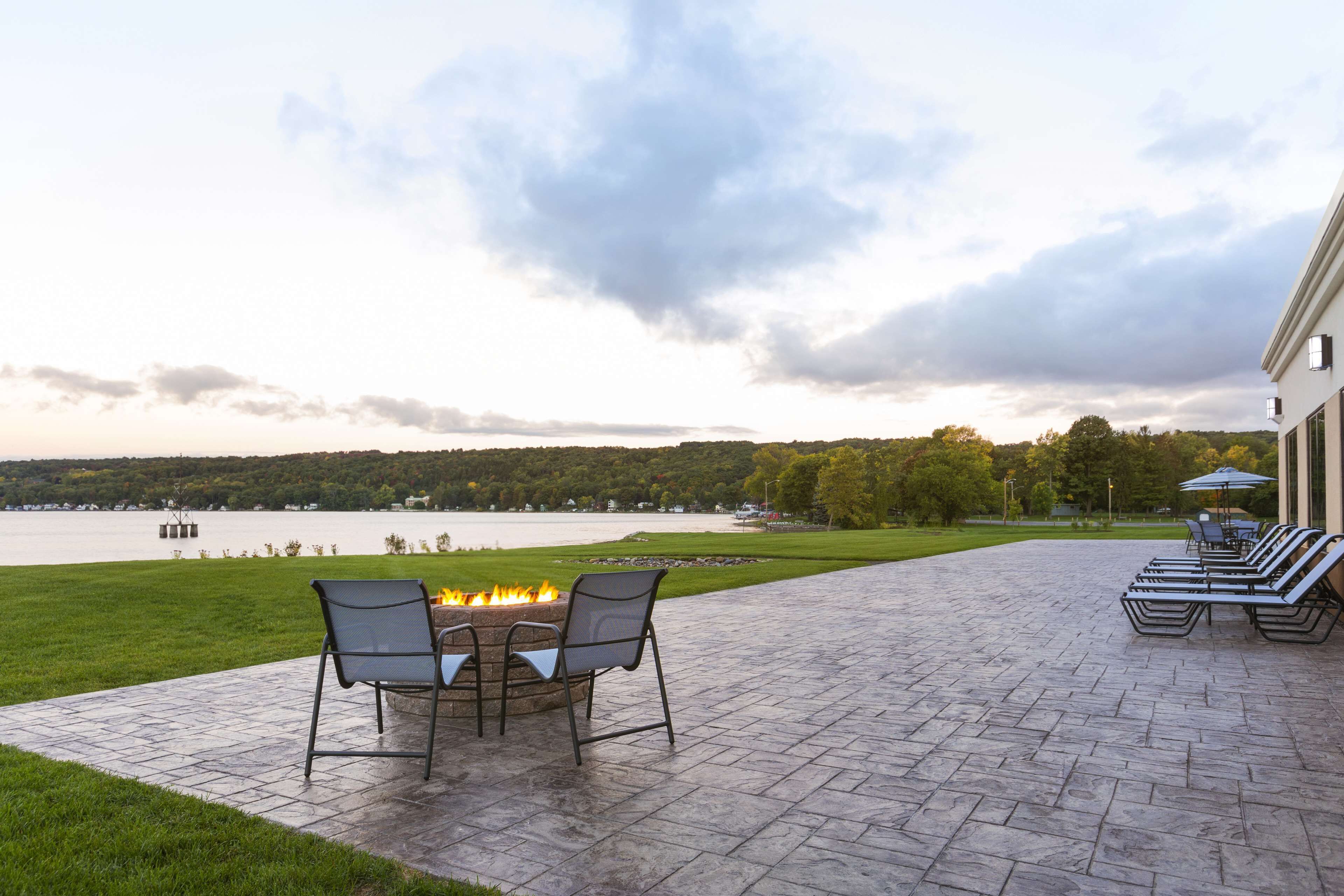 A patio with a fire pit, outdoor seating, and a view of a lake and trees.