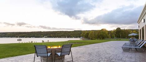 A patio with a fire pit, outdoor seating, and a view of a lake and trees.