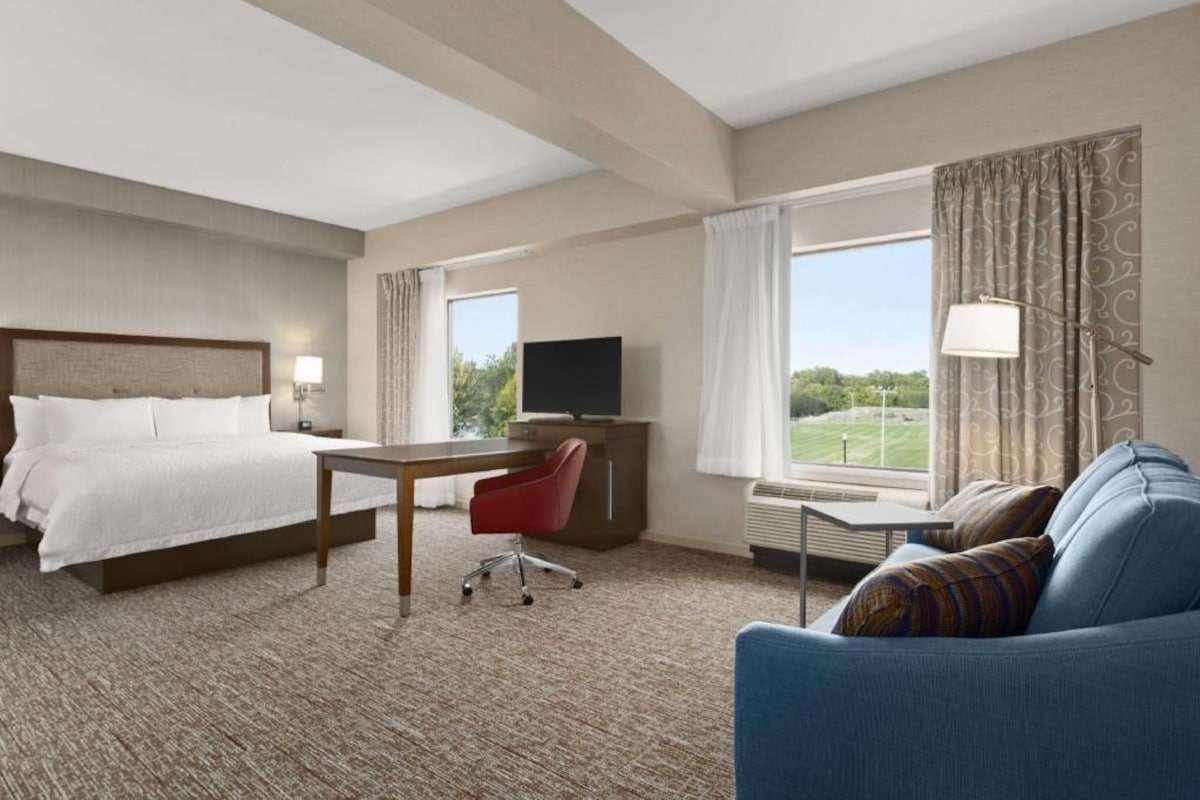 A hotel room with a bed, desk, TV, and a view of the outdoors.