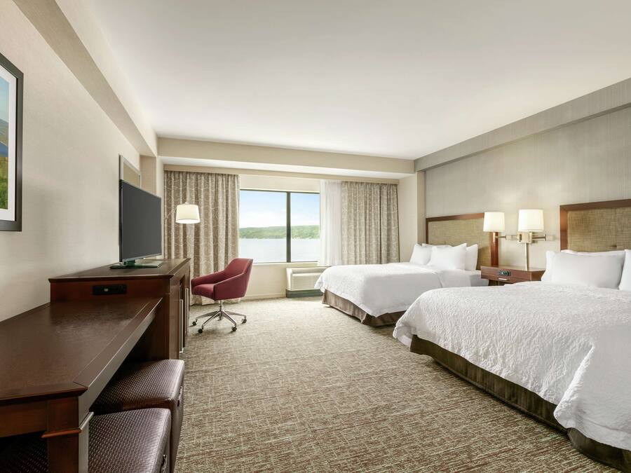 A hotel room with two beds, a desk, a chair, and a TV.