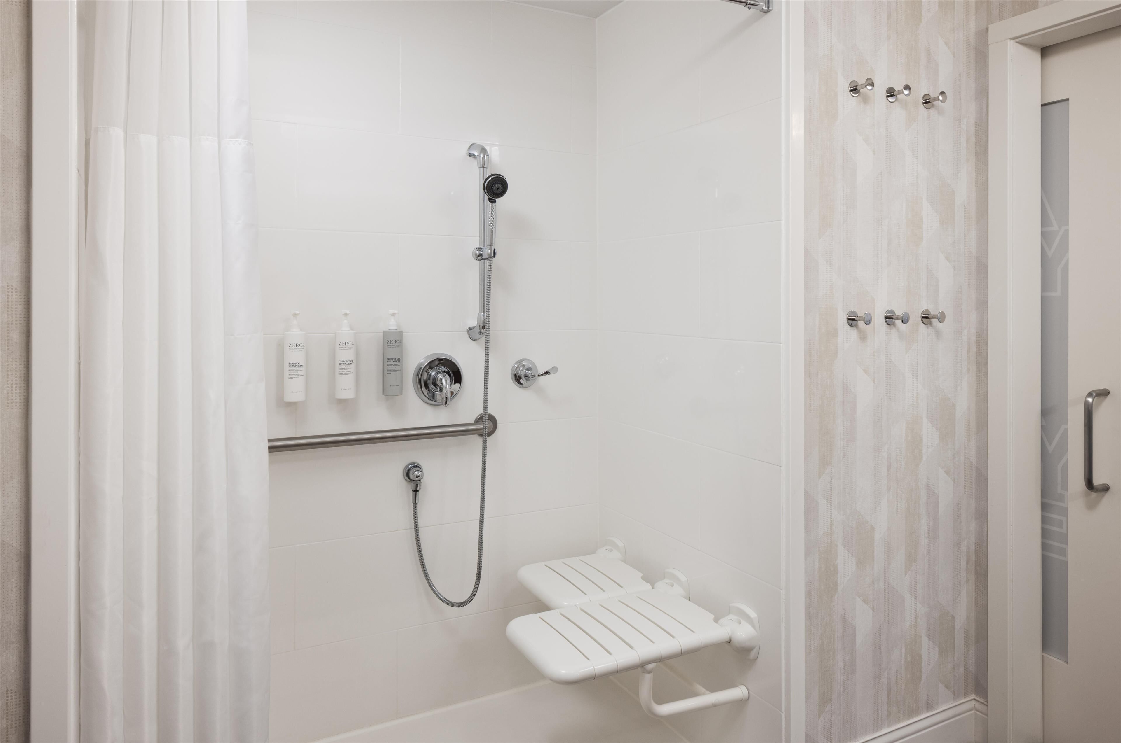 A walk-in shower with a handheld showerhead, a handheld shower attachment, and a white shower seat.