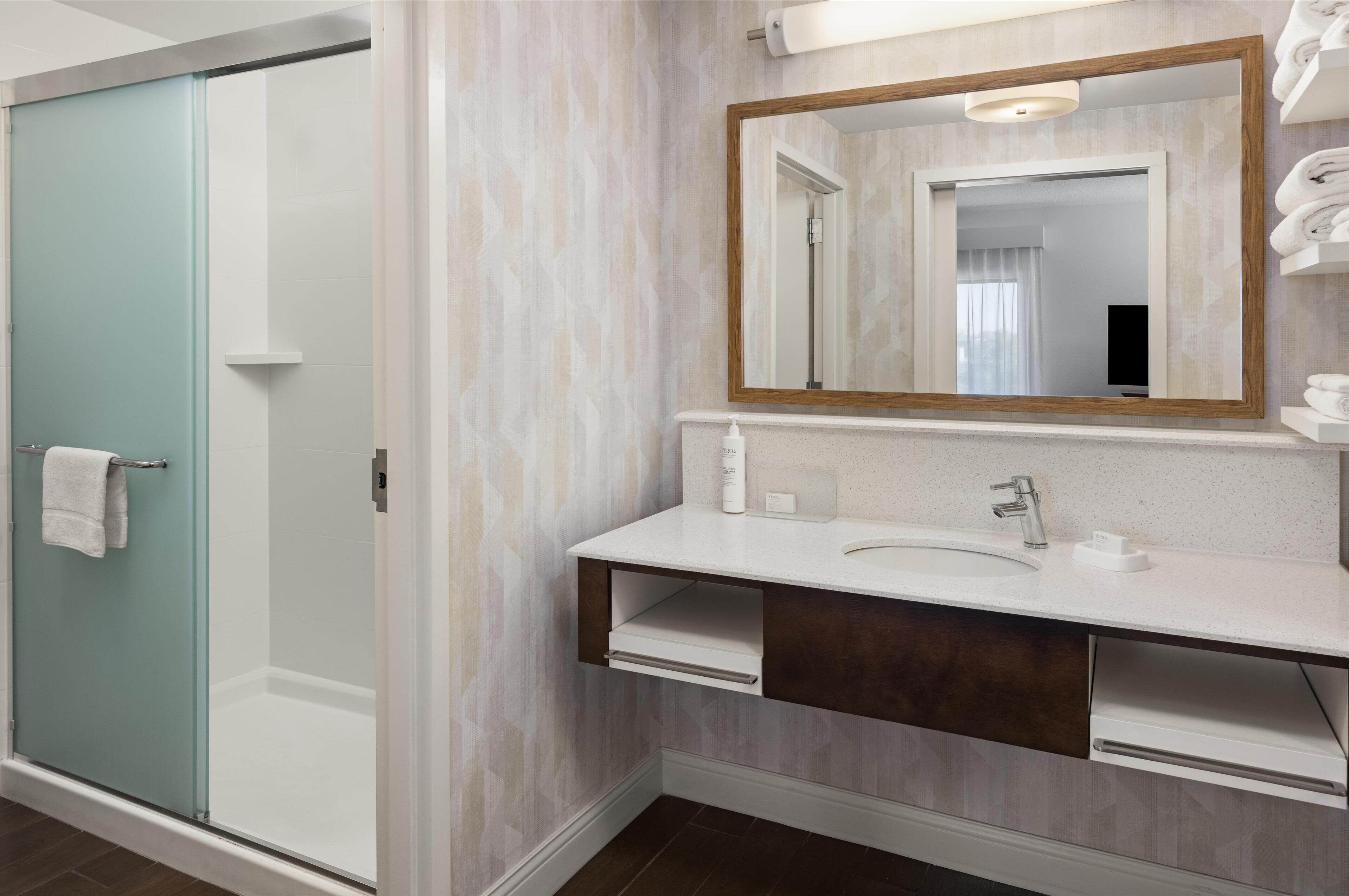 A bathroom with a shower, a sink, a mirror, and a towel rack.
