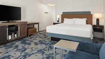 A hotel room with a bed, a TV, a desk, a lamp, and a sofa.