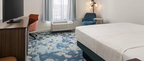 Habitación de hotel con cama, escritorio, televisor de pantalla plana, silla, lámpara de pie y ventana con cortinas.