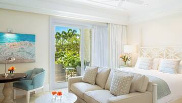 A hotel room with a bed, a sofa, a small table with flowers, a chair, and a painting of a beach scene.