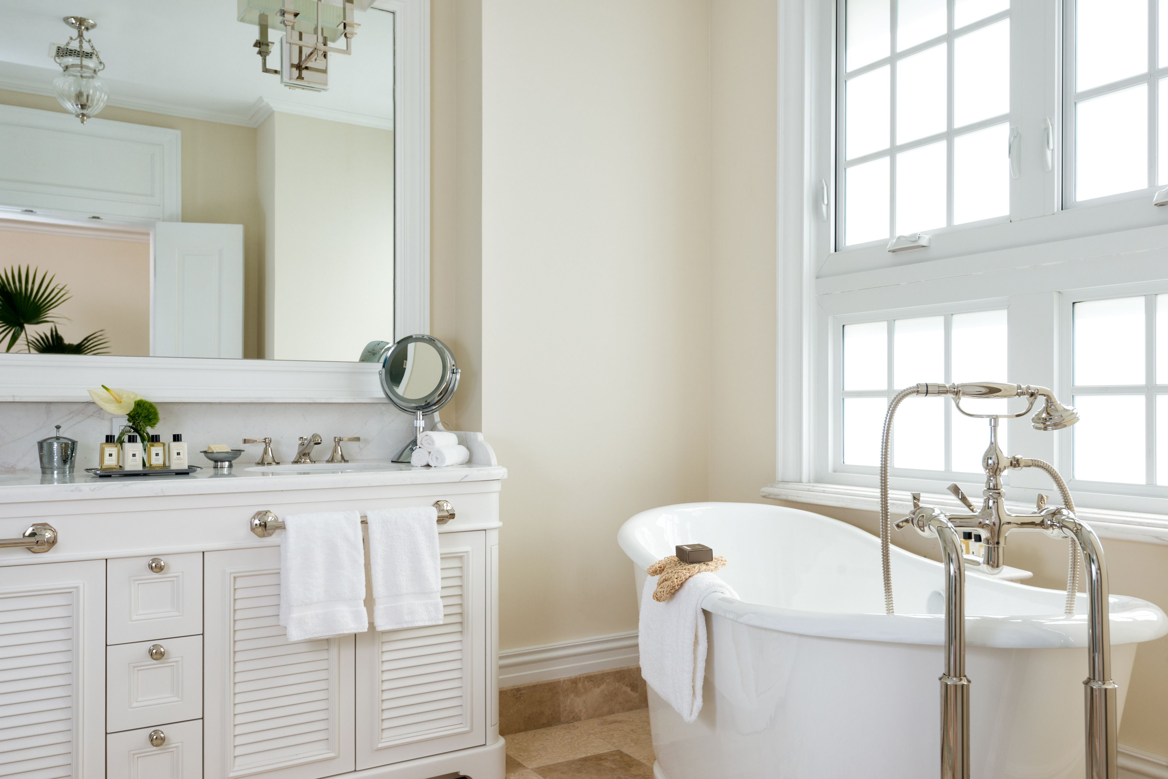 A bathroom with a white vanity, a large mirror, and a freestanding bathtub.