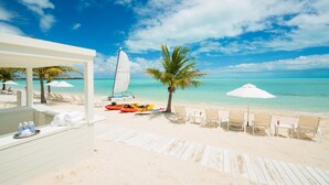 A beachside area with a lounge chair, a small table, and a sailboat.