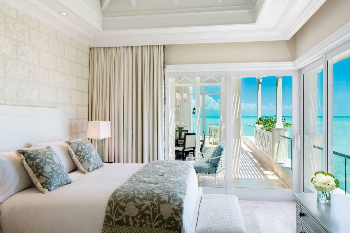 Habitación de hotel con una cama grande, un balcón con vistas al mar y una zona de comedor con mesa y sillas.