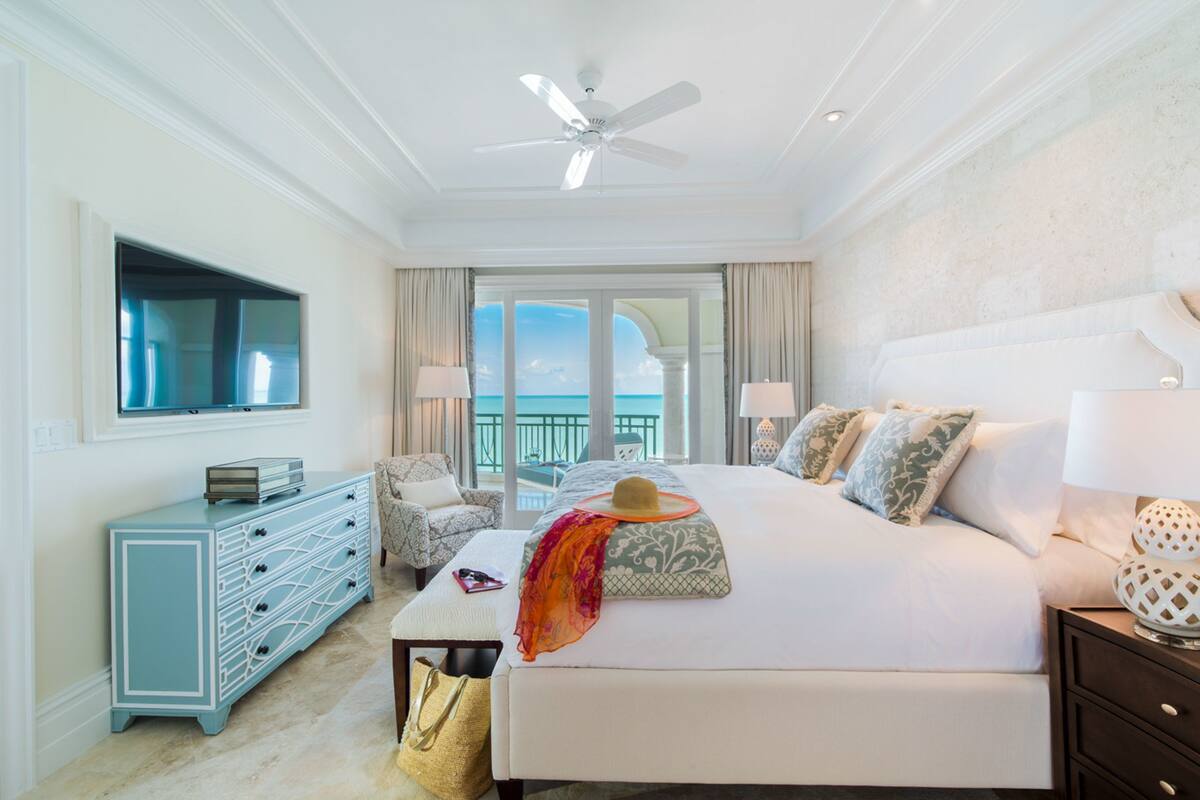 Un dormitorio amplio con una cama grande, ventilador de techo, televisión, cómoda y vistas al océano.