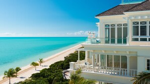 A beachfront property with a balcony overlooking the ocean, a white exterior, and a clear view of the beach.