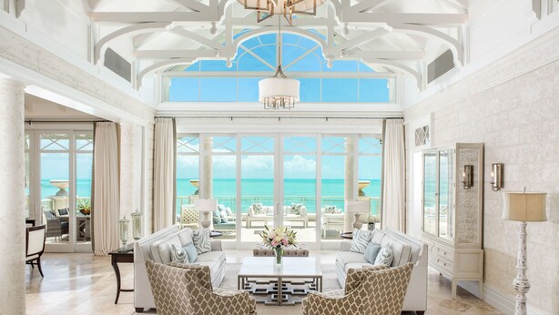 A spacious living room with a large window overlooking the ocean, a chandelier, and a dining area with a view.