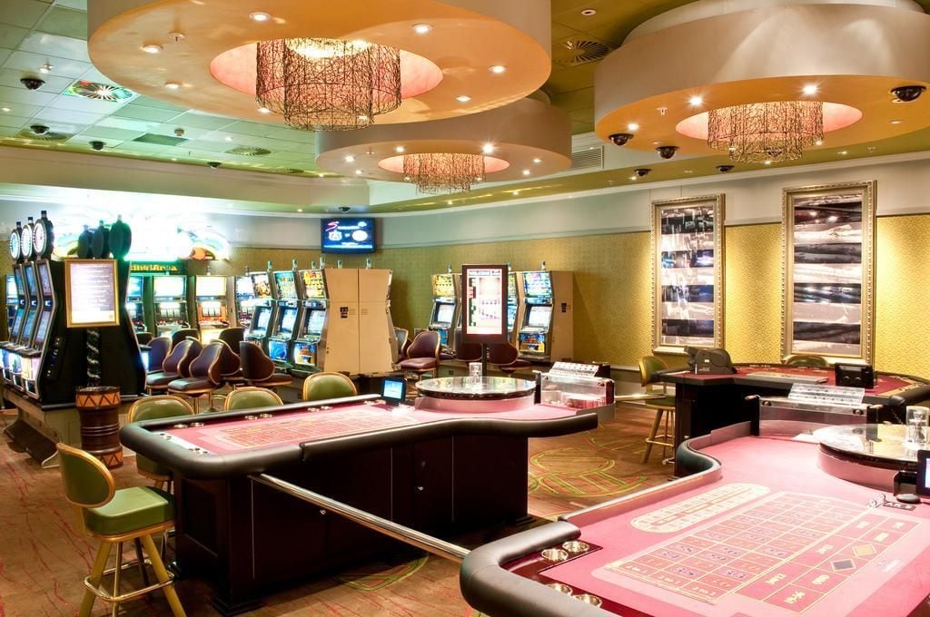A casino with slot machines, blackjack tables, and a large chandelier.