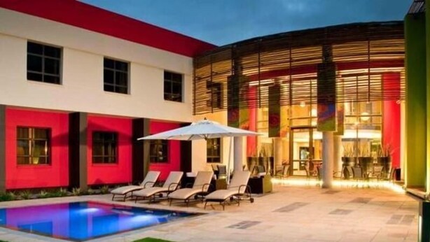 A modern building with a pool area, lounge chairs, and a covered seating area. - Peermont Metcourt at Umfolozi (Empangeni)