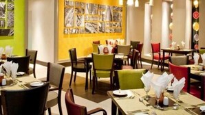 Ein Restaurantinnenraum mit mehreren Tischen und Stühlen, einer Wand mit gerahmten Kunstwerken und einer roten Akzentwand.