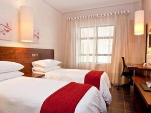 Une chambre d’hôtel avec deux lits, un bureau et une fenêtre avec des rideaux.