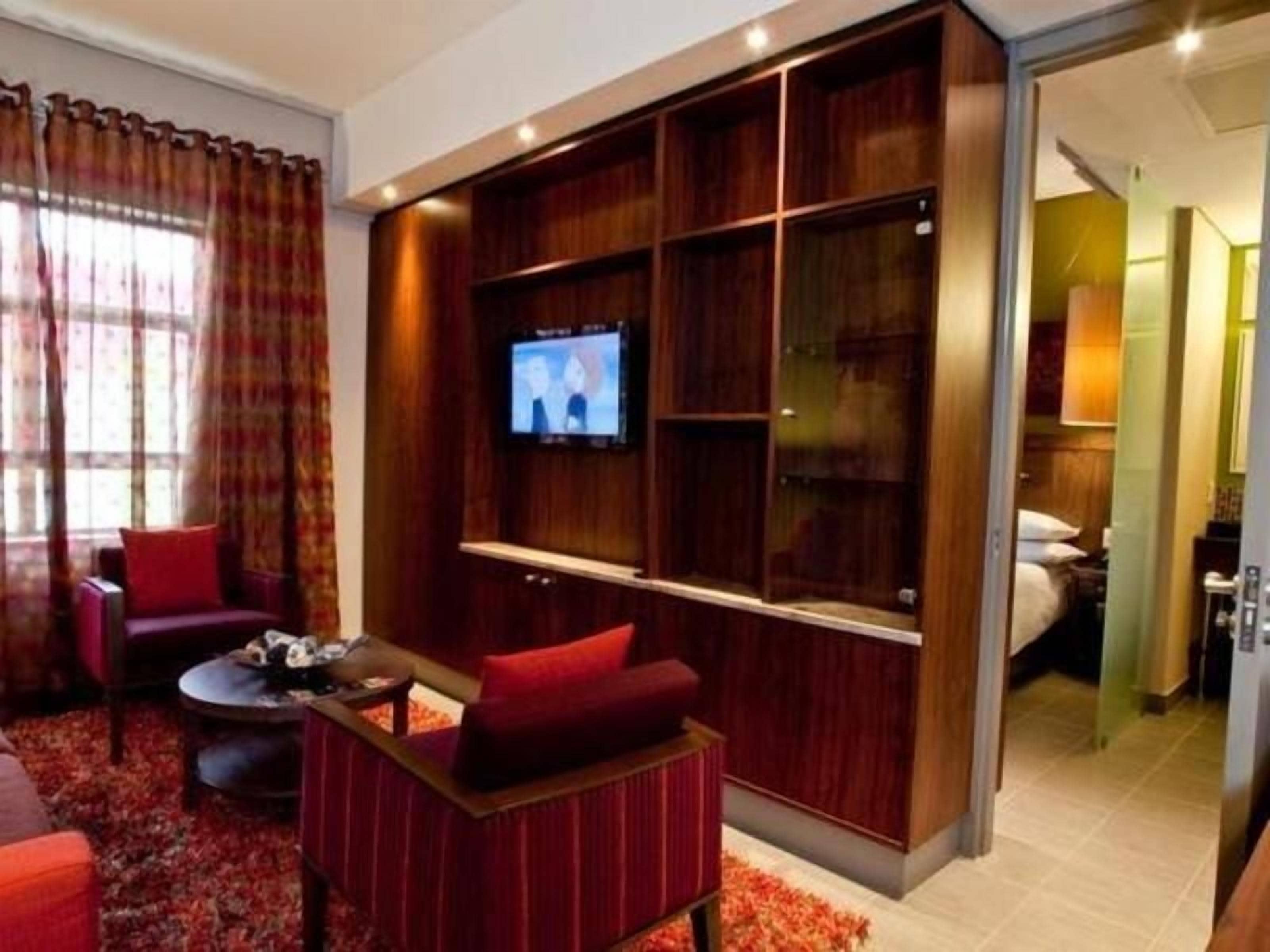 A modern living room with a flat-screen TV, red upholstered furniture, and a built-in entertainment unit.