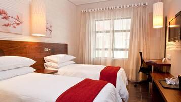 A hotel room with two beds, a desk, a chair, and a TV.