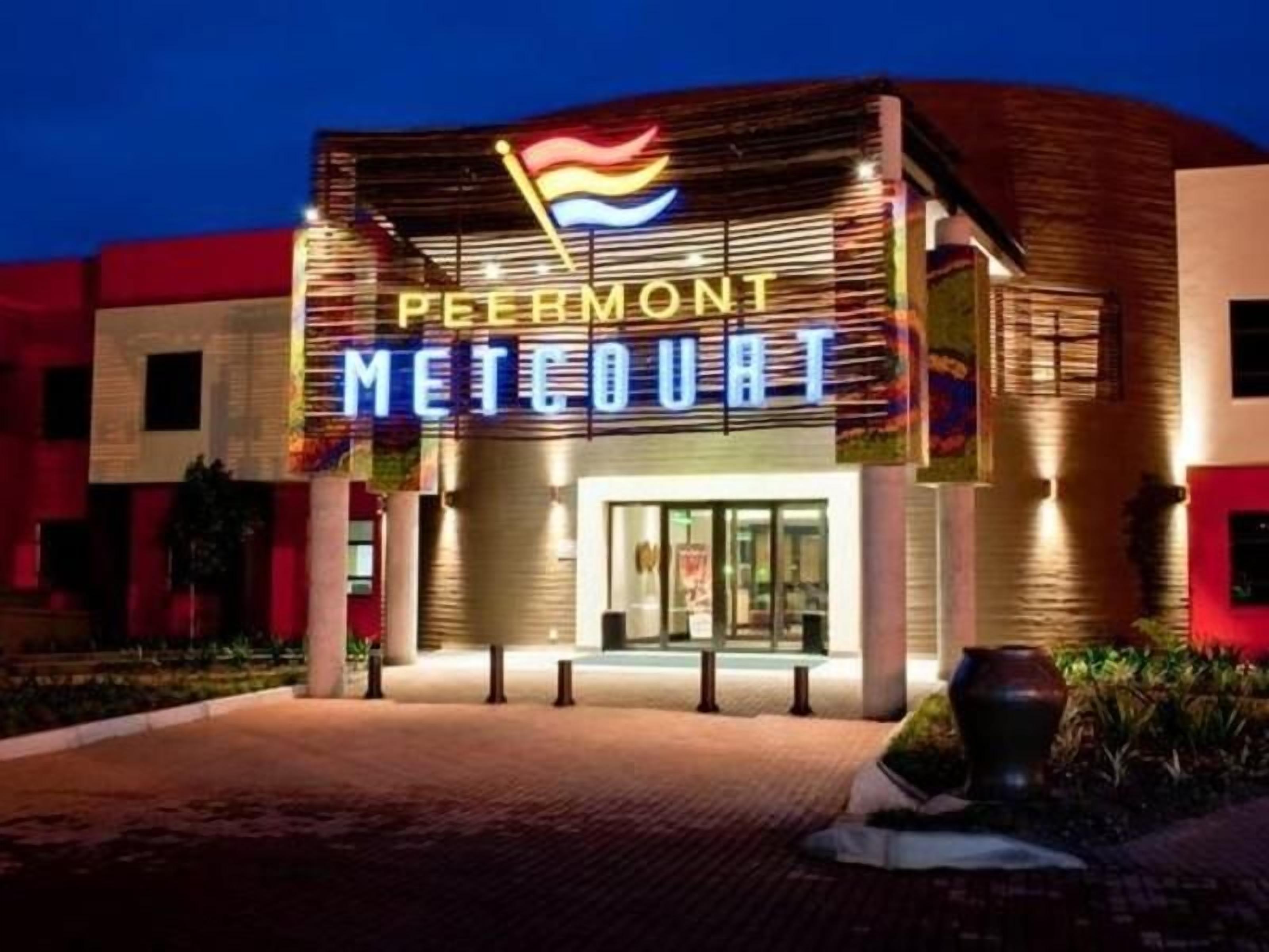 L’entrée d’un hôtel, avec une enseigne lumineuse au néon indiquant « PEIRMONT METCOURT ».