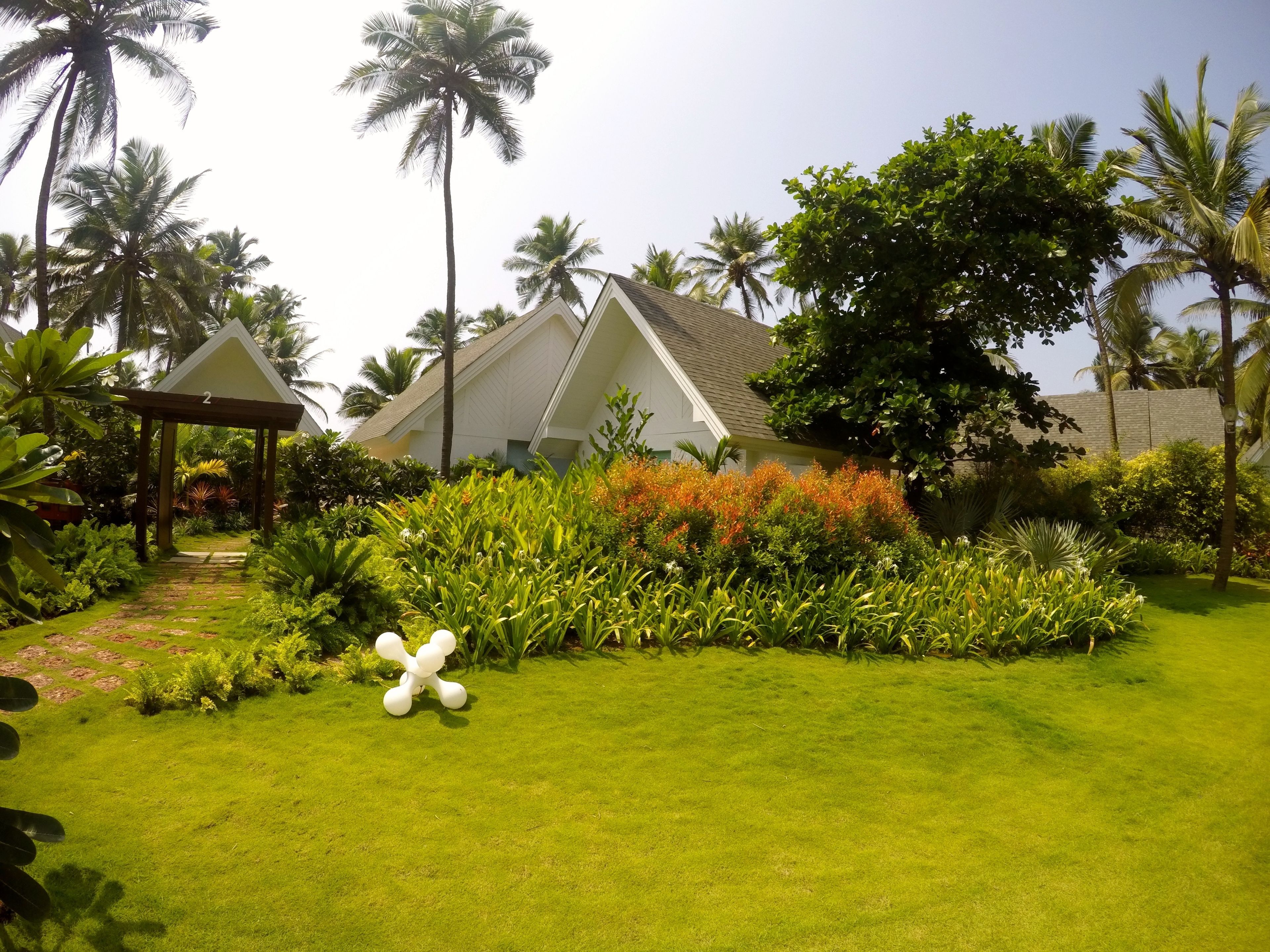 A well-maintained garden with a gazebo, palm trees, and a white building with a triangular roof.