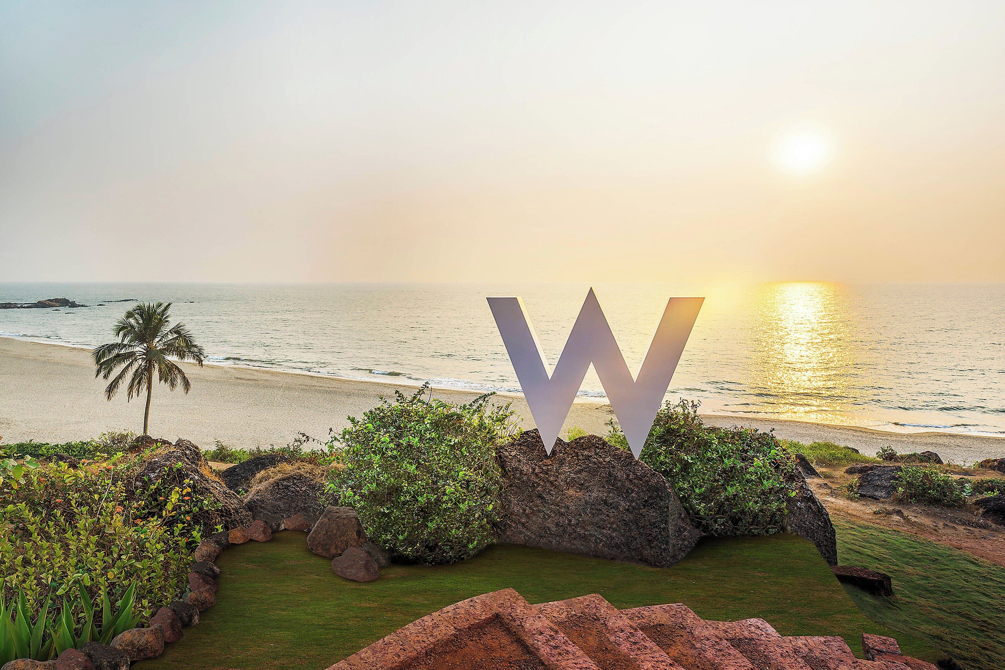 A beach view with a large 'W' sign, palm trees, and rocky terrain.