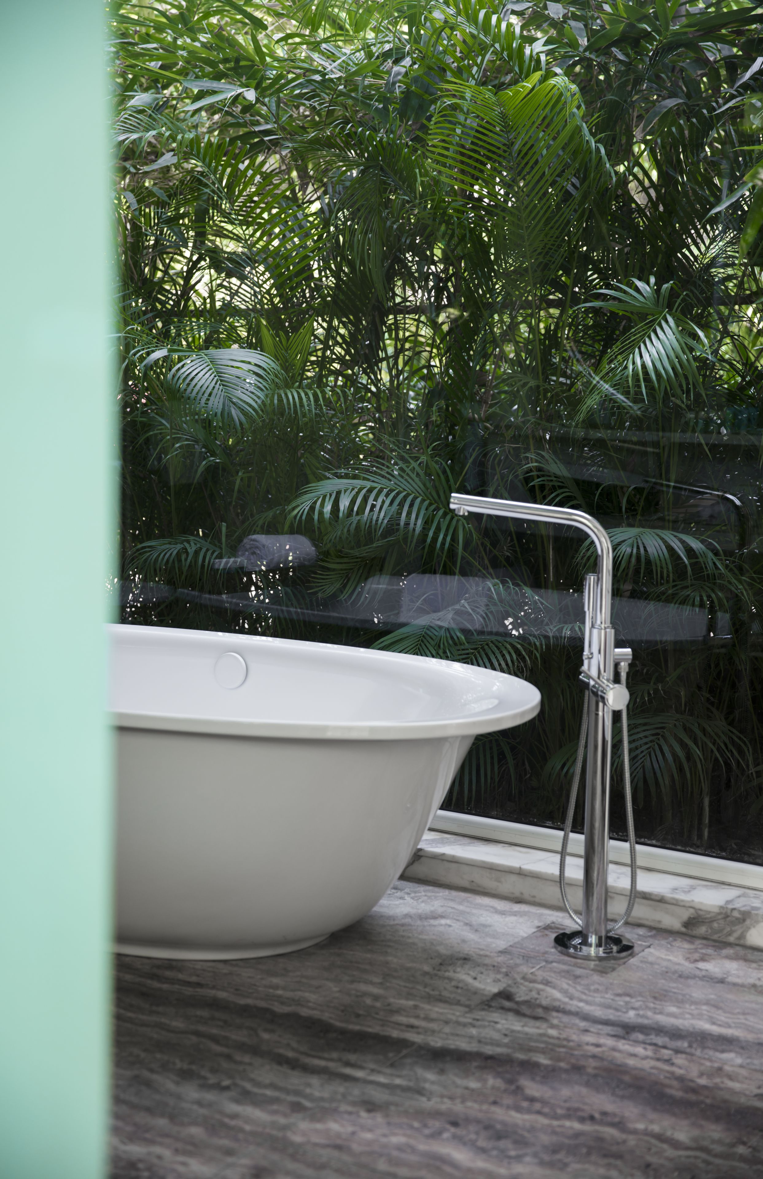 Una bañera con un grifo moderno, ubicada cerca de una ventana con vistas a un follaje verde exuberante.