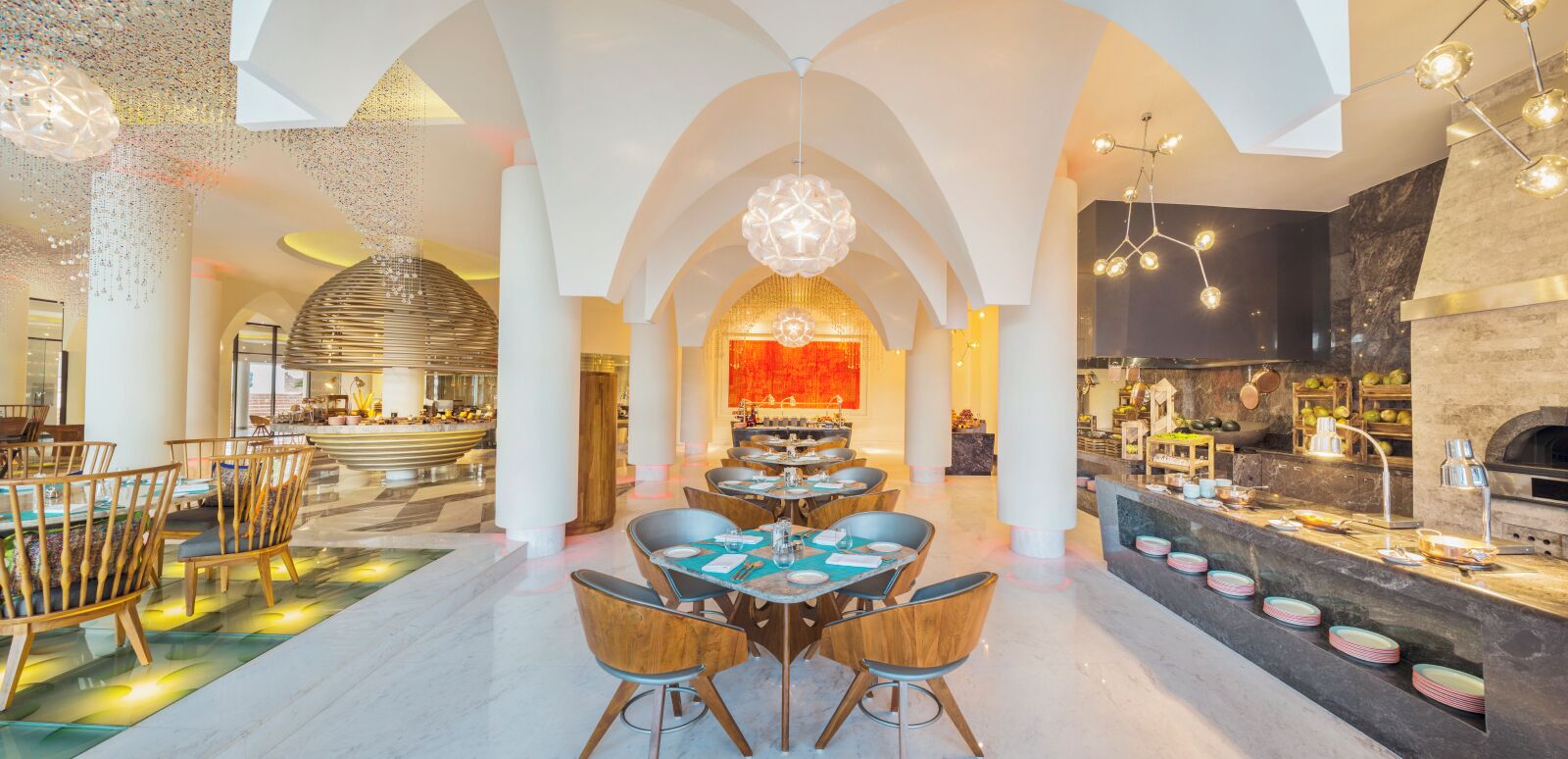 A spacious restaurant with high ceilings, modern chandeliers, and a central seating area with tables and chairs.