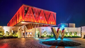 Un edificio moderno con fachada geométrica y una llamativa estructura iluminada en forma de 'W' al frente.