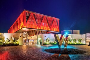 Un edificio moderno con fachada geométrica y una llamativa estructura iluminada en forma de 'W' al frente.