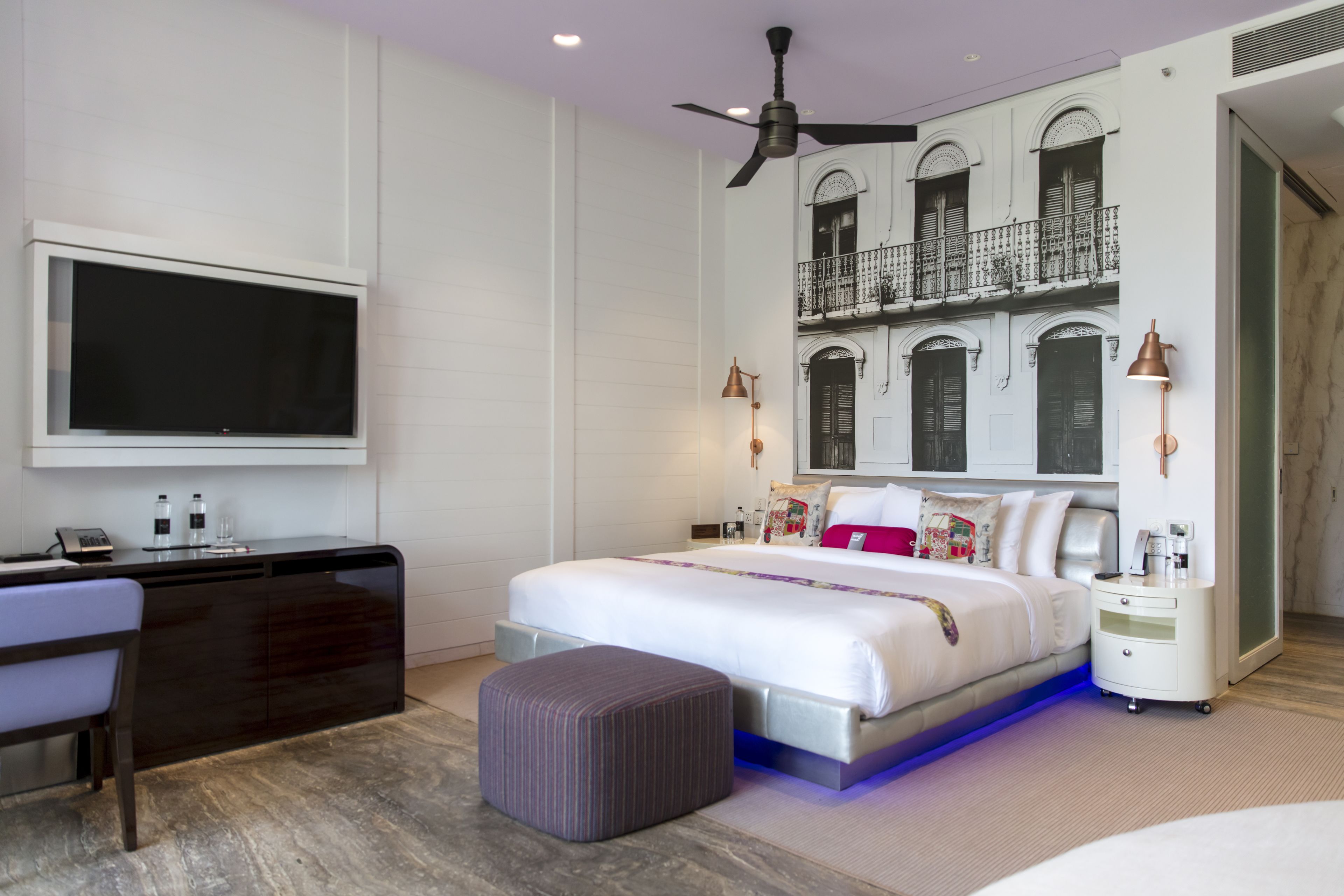 Quarto de hotel moderno com uma cama grande, uma escrivaninha, televisão e varanda com grades decorativas.