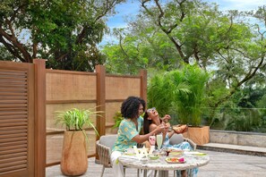 An outdoor dining area with a table set for two, surrounded by lush greenery and a wooden fence.