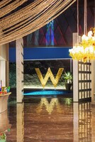 Un lobby lujoso con un gran letrero dorado con la letra 'W', un piso reflectante y un candelabro.