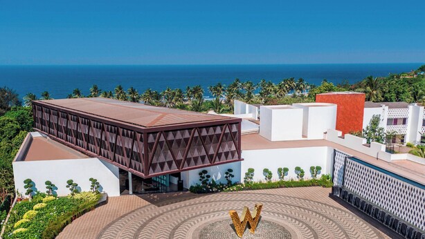 A modern building with a large 'W' logo, surrounded by lush greenery and a view of the ocean.